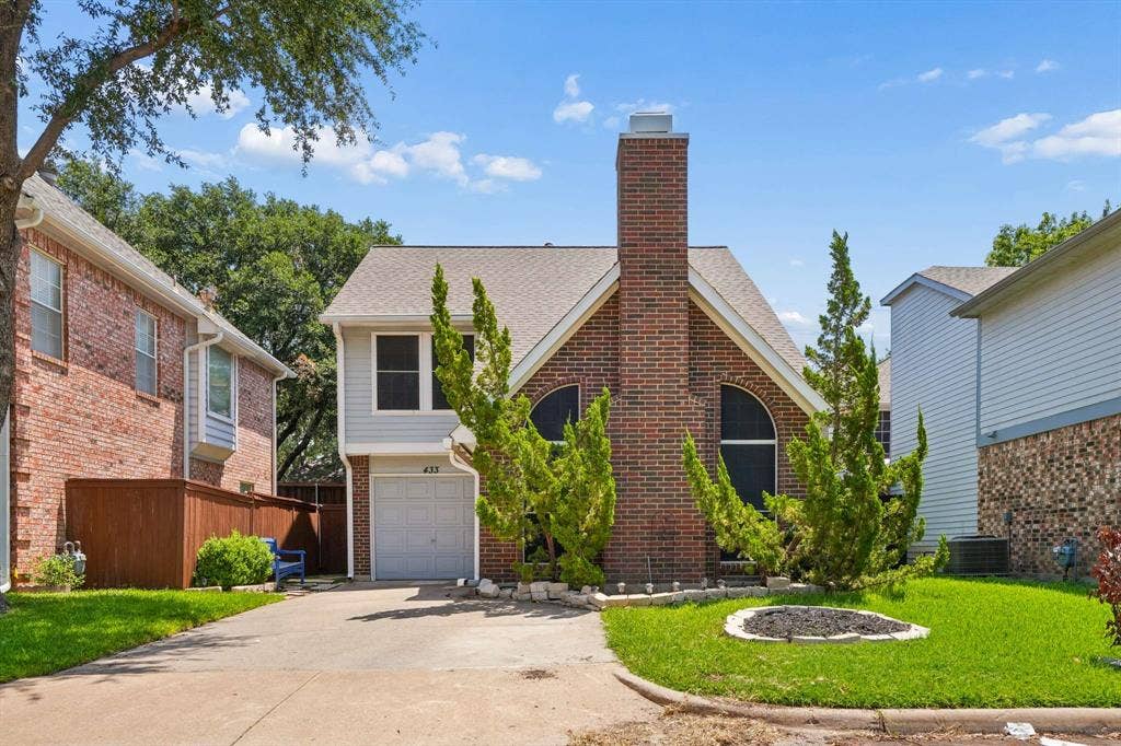 Brick and siding exterior featuring an attached garage, a prominent brick chimney, and decorative arched windows