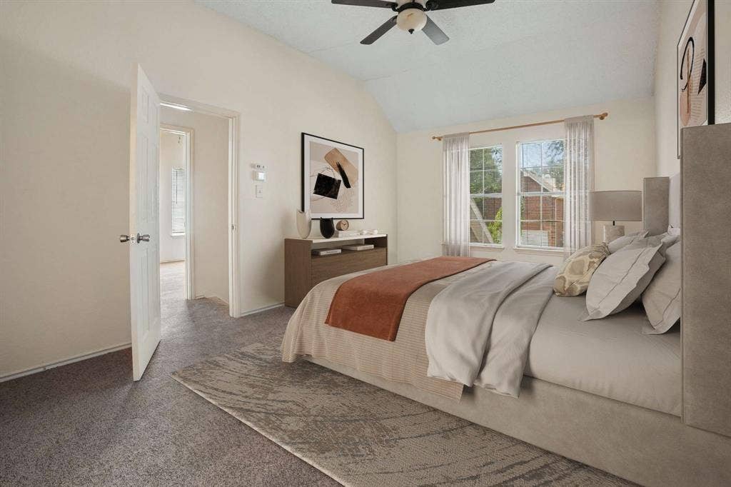 Carpeted bedroom featuring vaulted ceilings, a ceiling fan, two windows with curtains, and a solid core door