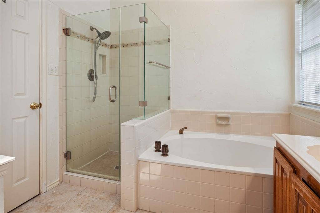 Bathroom featuring a glass-enclosed shower, built-in bathtub, and a window with blinds