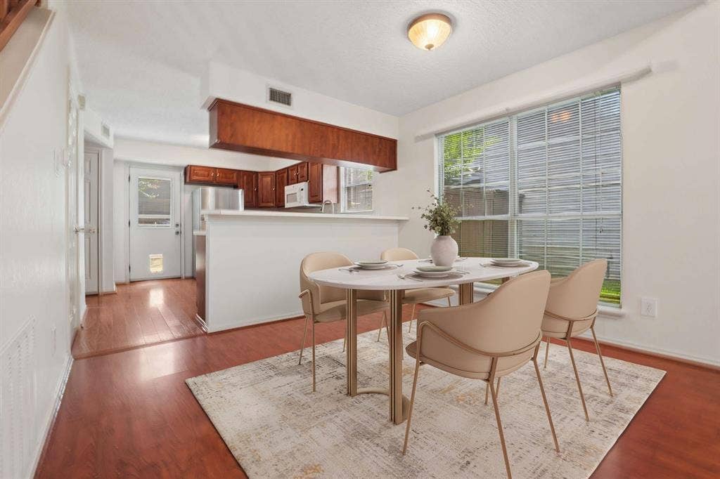 Open-concept dining area with wood-finish flooring, a large window with blinds, and white walls