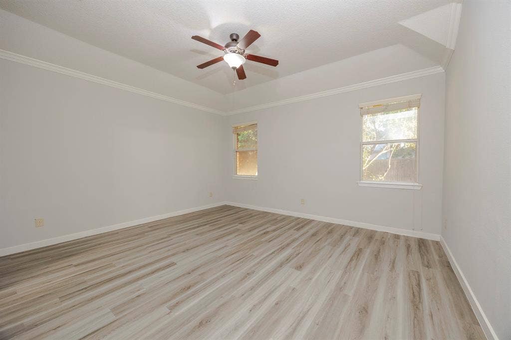 12475 Cajun Drive, Frisco, TX 75035 Tray ceiling with crown molding, wood-finish flooring, two windows, and a ceiling fan with integrated lighting