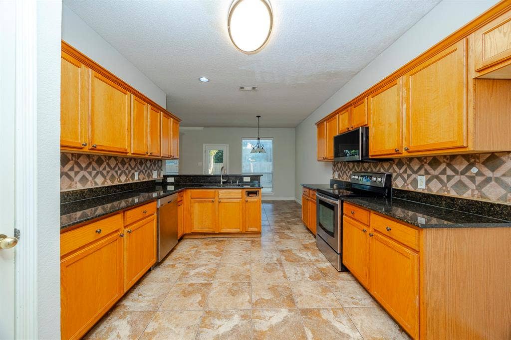 12475 Cajun Drive, Frisco, TX 75035 Kitchen featuring wood cabinetry, dark countertops, a patterned tile backsplash, stainless steel appliances, and large format tile flooring