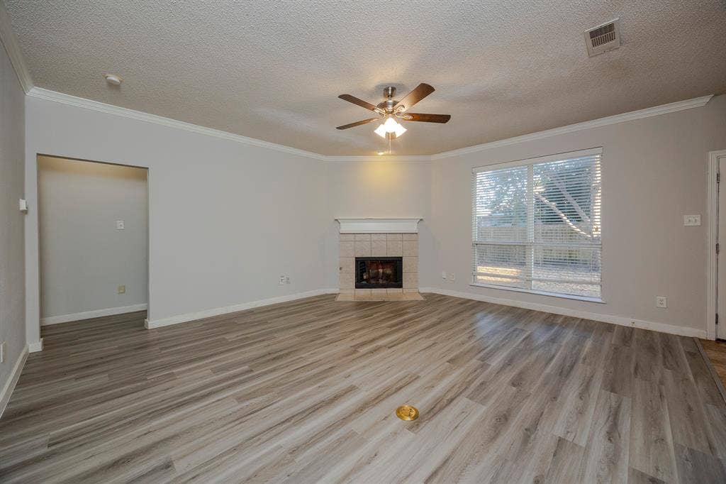 12475 Cajun Drive, Frisco, TX 75035 Spacious living area featuring wood-finish flooring, a tiled fireplace with mantel, a ceiling fan with integrated lighting, and crown molding