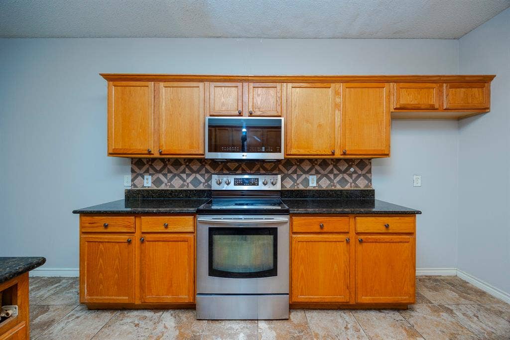 12475 Cajun Drive, Frisco, TX 75035 Wood-finish cabinetry, dark speckled countertops, stainless steel range, and built-in microwave
