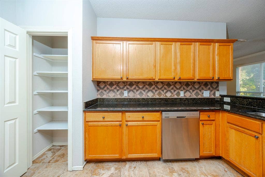 12475 Cajun Drive, Frisco, TX 75035 Kitchen featuring wood cabinetry, dark countertops, tiled backsplash, stainless steel dishwasher, and pantry with shelving