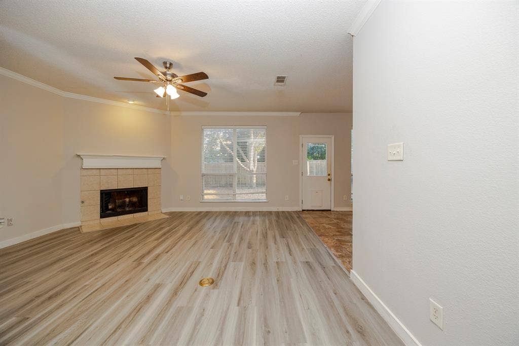 12475 Cajun Drive, Frisco, TX 75035 Living area featuring wood-finish flooring, a tile-surround fireplace with a mantel, crown molding, and a ceiling fan with integrated lighting