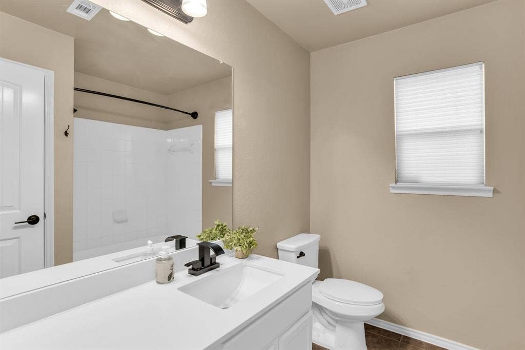 805 Andrews Court, Anna, TX 75409 Bathroom featuring a white vanity with integrated sink, black fixtures, a wall-mounted mirror, white toilet, and a window with blinds. All updated.