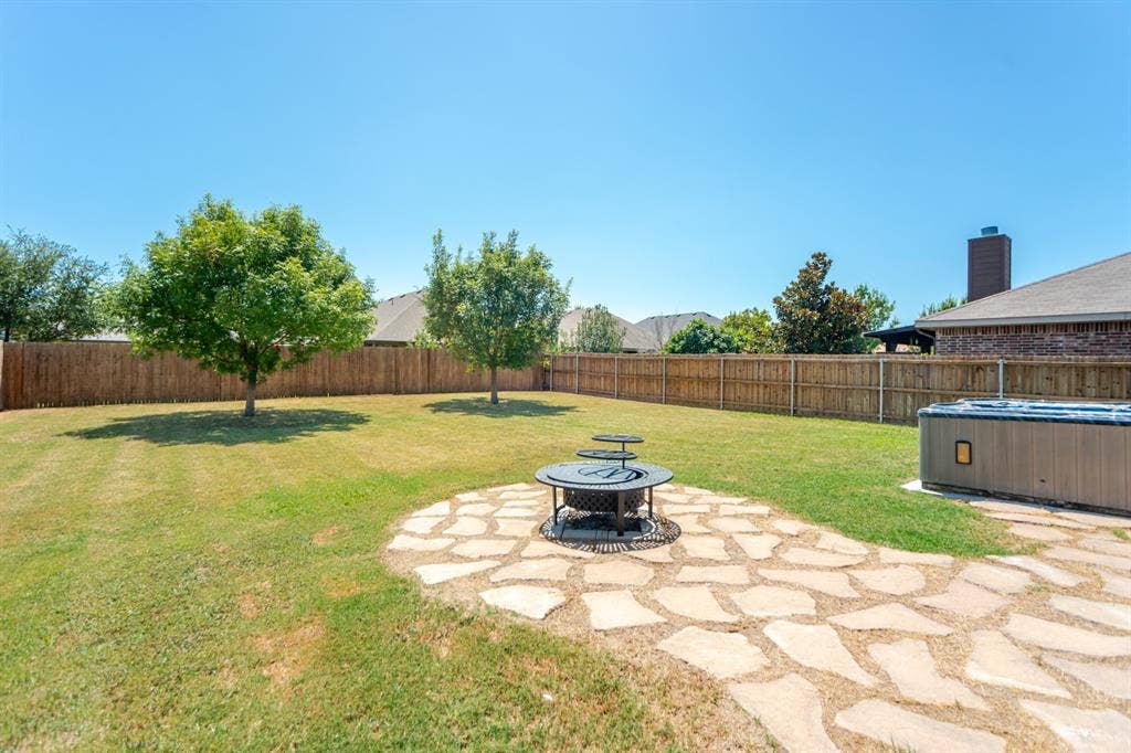 805 Andrews Court, Anna, TX 75409 Spacious backyard with a wood privacy fence, flagstone patio, fire pit, and a hot tub