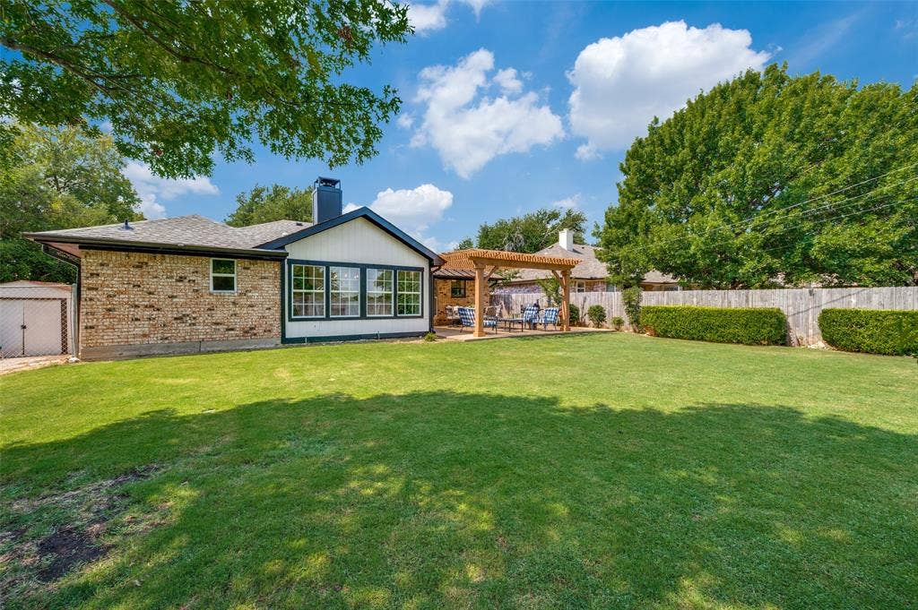 8420 Christie Drive, Frisco, TX 75033 Backyard has lots of play space, a brick and white siding exterior, multiple windows, a dedicated patio area with a wooden pergola, and with a storage building tucked away from the main views