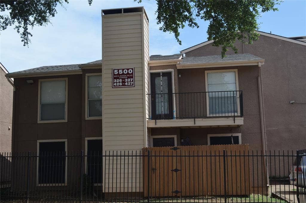 5500 Boca Raton Boulevard, #426, Fort Worth, TX 76112 Two-story exterior featuring a private balcony with black metal railing, a prominent chimney with horizontal siding, and a black metal fence enclosing a private patio area