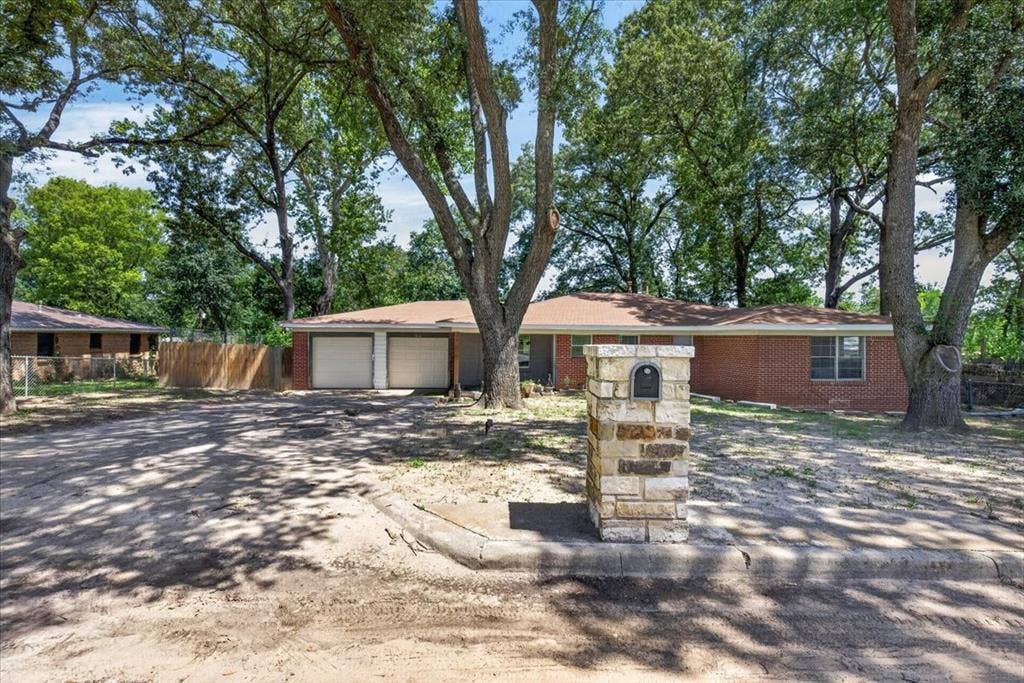 925 Maryland Drive, Athens, TX 75751 Brick exterior residence featuring a two-car garage with individual doors, a stone-clad mailbox pillar, and mature trees providing natural shade