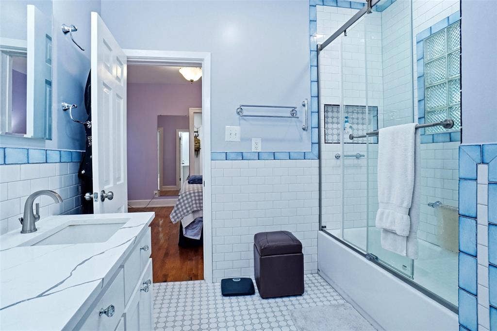 2306 Western Avenue, Fort Worth, TX 76107 Bathroom featuring a white subway tile surround with blue accent tiles, a single vanity with a white countertop and undermount sink, and a combination tub and shower with a glass enclosure