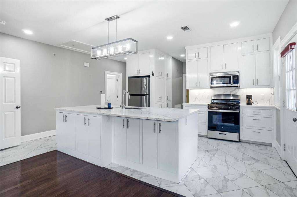 2306 Western Avenue, Fort Worth, TX 76107 Kitchen featuring white cabinetry, stainless steel appliances, a center island with sink, marble-finish countertops, and patterned tile flooring