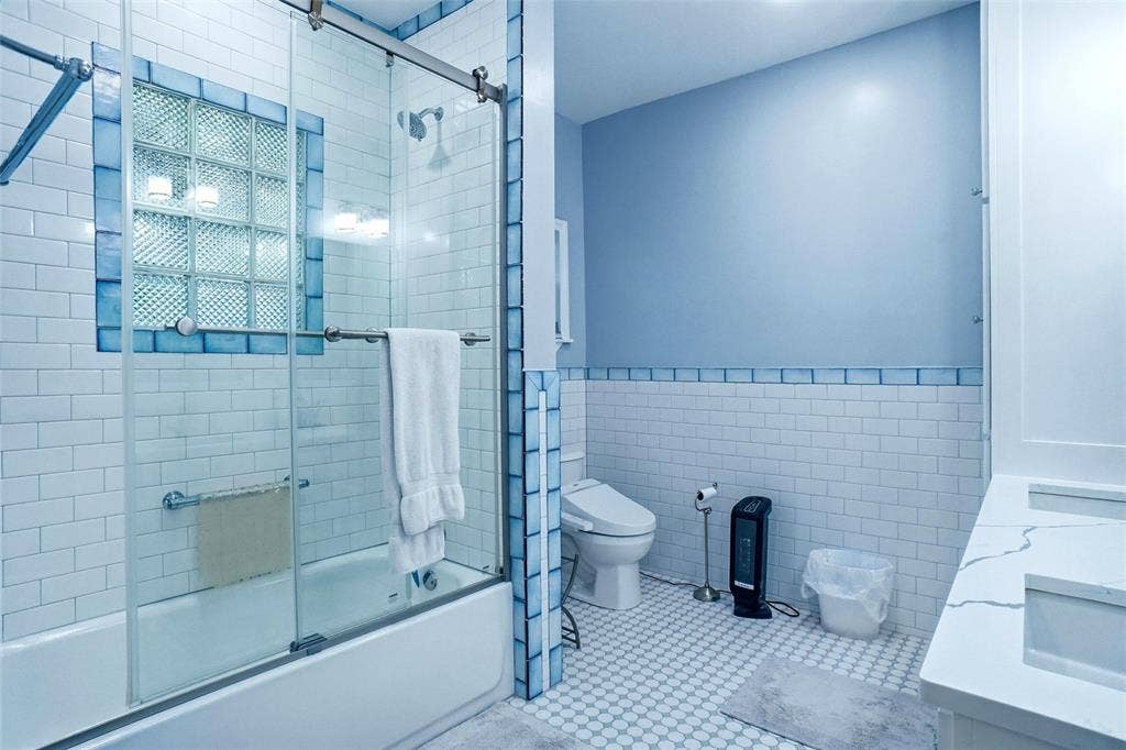 2306 Western Avenue, Fort Worth, TX 76107 Bathroom featuring a tiled tub-shower combination with glass enclosure, glass block window, and blue accent tiles