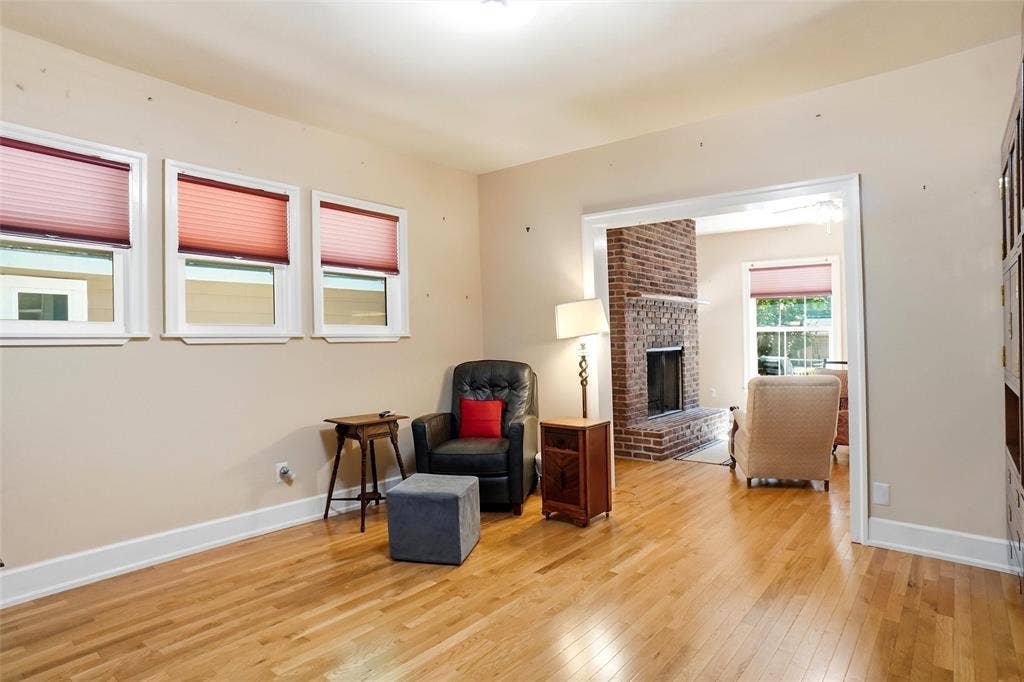 2306 Western Avenue, Fort Worth, TX 76107 Hardwood flooring extends throughout this room, featuring three windows with white trim and a wide doorway opening to a room with a brick fireplace