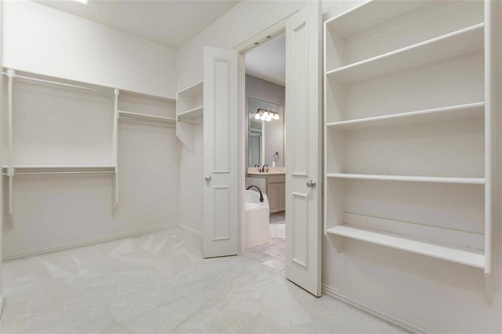 921 Pine Burst Drive, Allen, TX 75013 Spacious walk-in closet featuring white built-in shelving, hanging rods, and light-toned carpet flooring