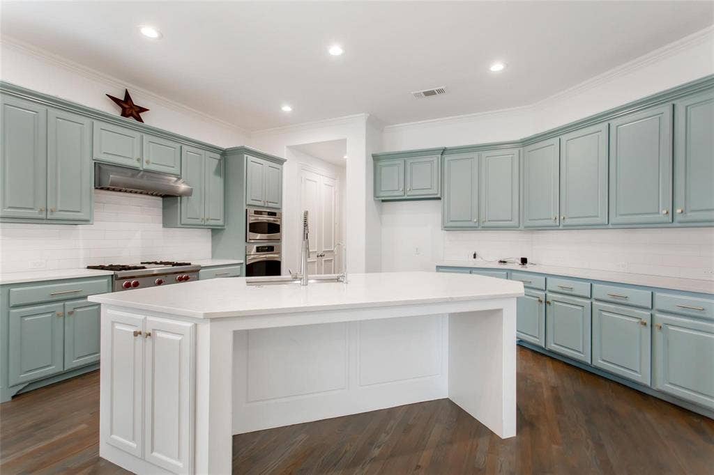 921 Pine Burst Drive, Allen, TX 75013 Modern kitchen featuring light blue cabinetry, a large central island with white countertops, stainless steel appliances, a subway tile backsplash, and dark wood-finish flooring