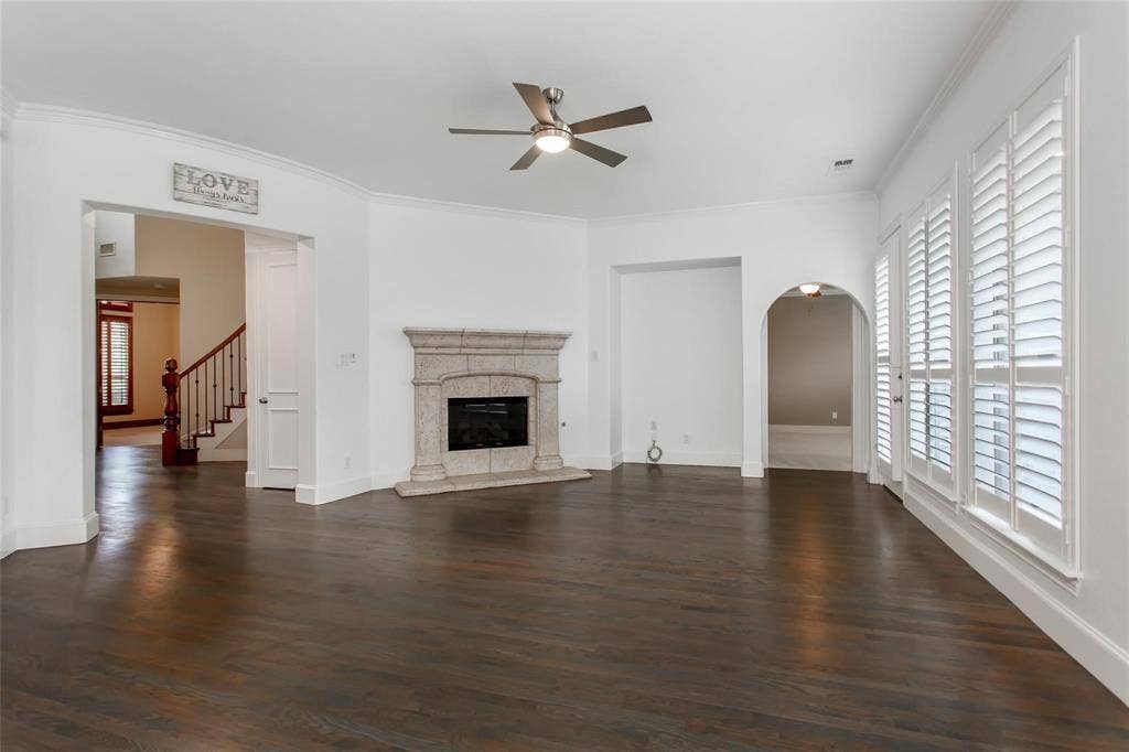 921 Pine Burst Drive, Allen, TX 75013 Spacious living area featuring dark wood-finish flooring, a stone-surround fireplace, and a ceiling fan