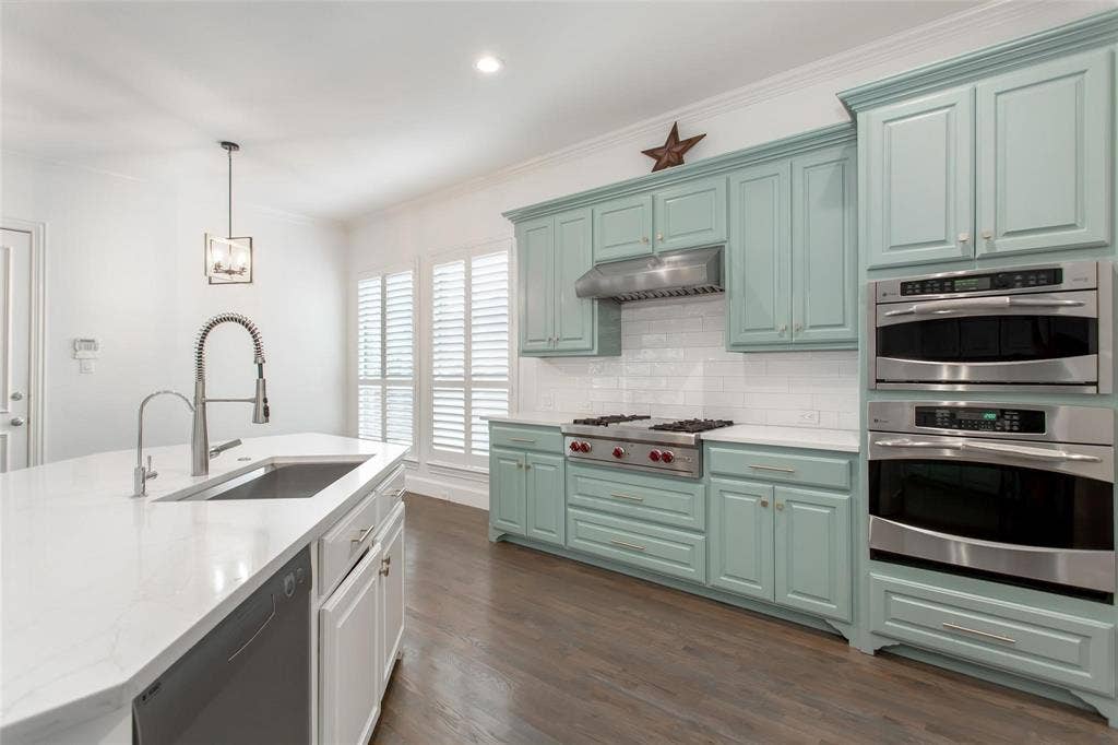 921 Pine Burst Drive, Allen, TX 75013 Kitchen featuring light teal cabinetry, stainless steel appliances, a gas range with range hood, white subway tile backsplash, and a center island with an undermount sink and gooseneck faucet