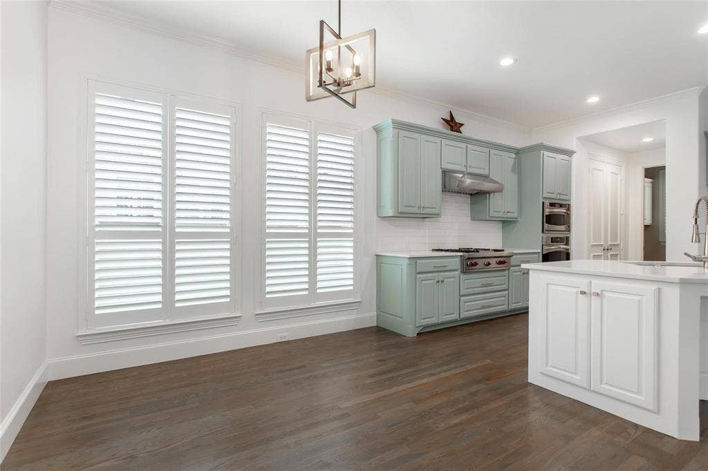 921 Pine Burst Drive, Allen, TX 75013 Expansive kitchen and dining area featuring wide plank wood-finish flooring, three large windows with plantation shutters, custom cabinetry, a built-in range, and a kitchen island with storage