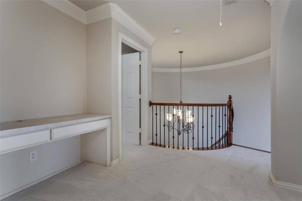 921 Pine Burst Drive, Allen, TX 75013 Upper-level landing featuring a built-in desk with two drawers, crown molding, and a curved staircase with wood newel posts and iron balusters