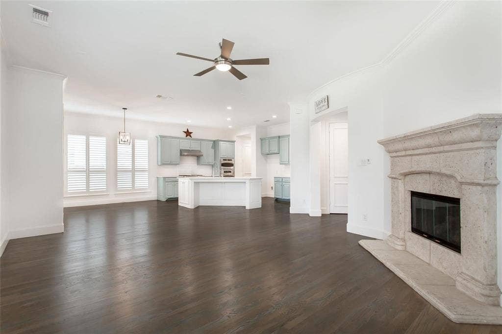 921 Pine Burst Drive, Allen, TX 75013 Expansive open-concept living space featuring dark wood-finish flooring, a stone fireplace, and crown molding