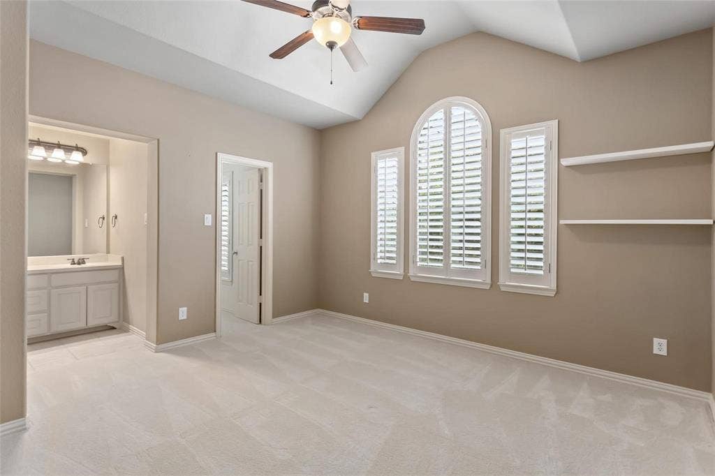 921 Pine Burst Drive, Allen, TX 75013 Vaulted ceiling with a ceiling fan, three windows with plantation shutters, light-toned carpeting, built-in shelving, and an en-suite vanity area with a built-in sink and light fixture