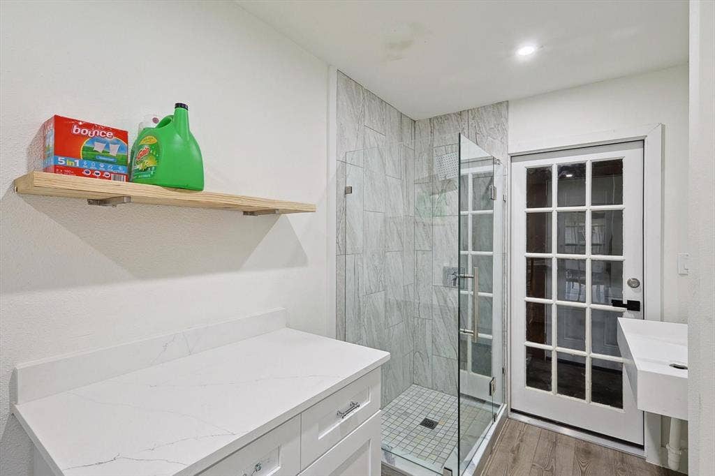1208 Mayleaf Drive, Irving, TX 75060 Laundry area featuring a built-in white vanity with a white countertop, a floating wood-finish shelf, and wood-finish flooring