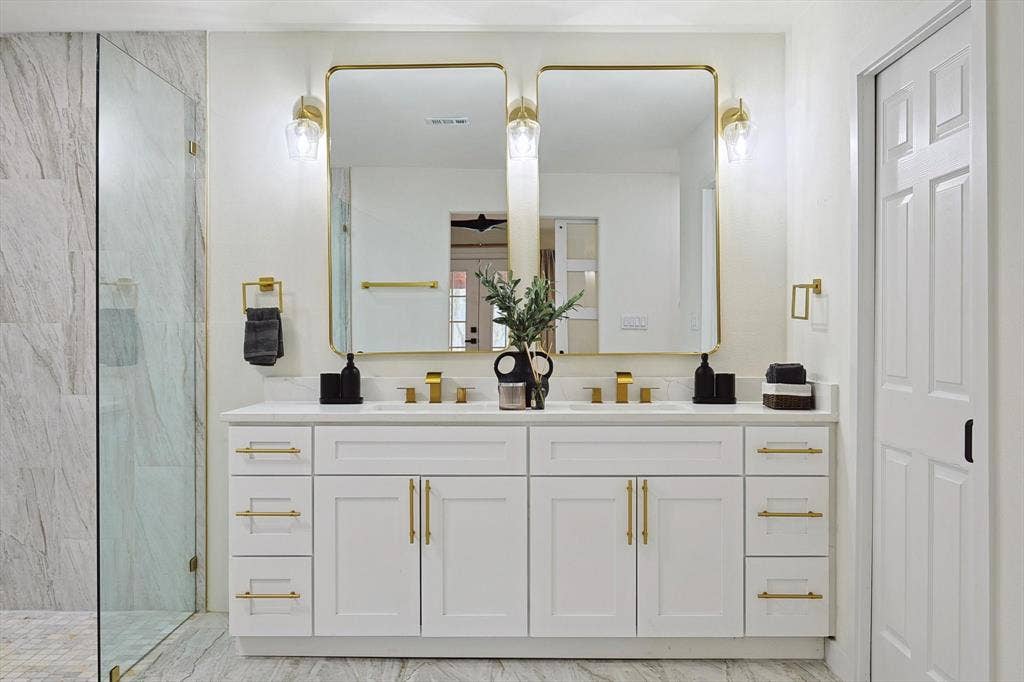 1208 Mayleaf Drive, Irving, TX 75060 Dual vanity with white cabinetry and gold-tone hardware, featuring a white countertop and gold-tone faucets