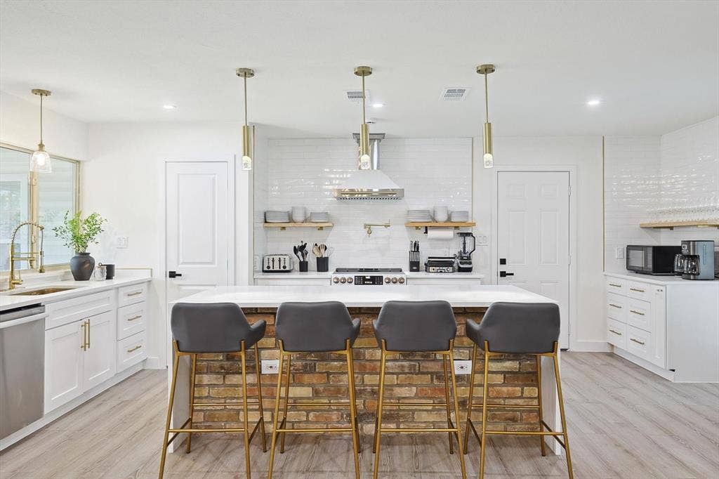 1208 Mayleaf Drive, Irving, TX 75060 Modern kitchen featuring a brick-clad island with seating, white shaker cabinetry, stainless steel appliances, white subway tile backsplash, and light wood-finish flooring