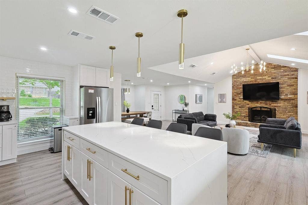 1208 Mayleaf Drive, Irving, TX 75060 Open-concept kitchen featuring a large central island with white cabinetry and brass hardware, complemented by light wood-finish flooring