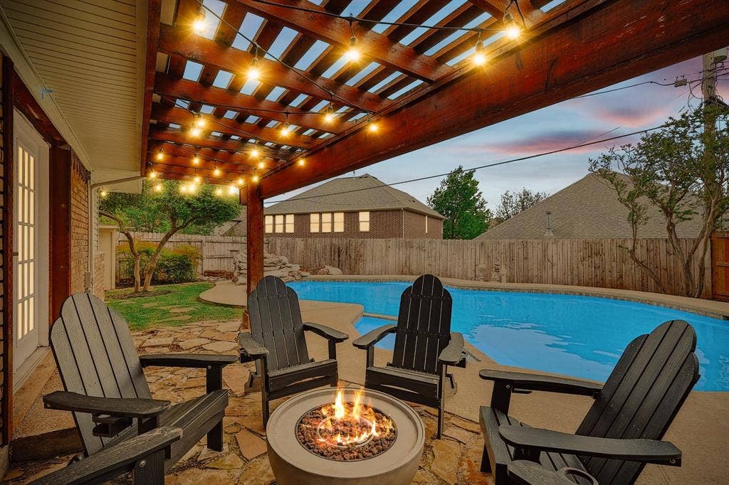 1208 Mayleaf Drive, Irving, TX 75060 Outdoor living area featuring a wood pergola with string lights, a stone patio, an in-ground swimming pool, and a fire pit