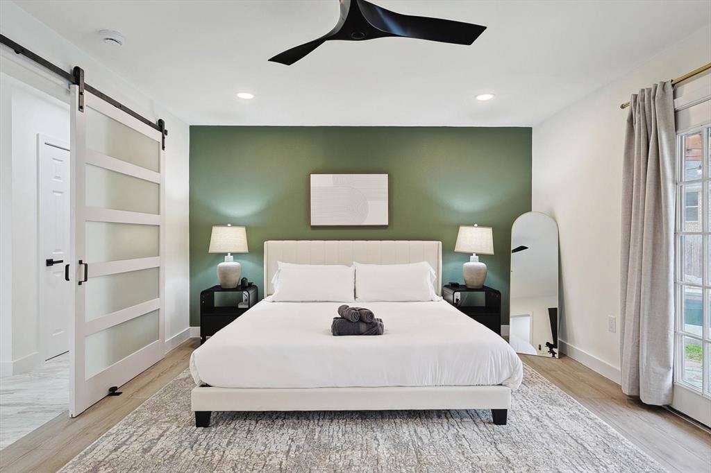 1208 Mayleaf Drive, Irving, TX 75060 Bedroom featuring a dark green accent wall, wood-finish flooring, a modern barn door with frosted glass panels, recessed lighting, and a black ceiling fan
