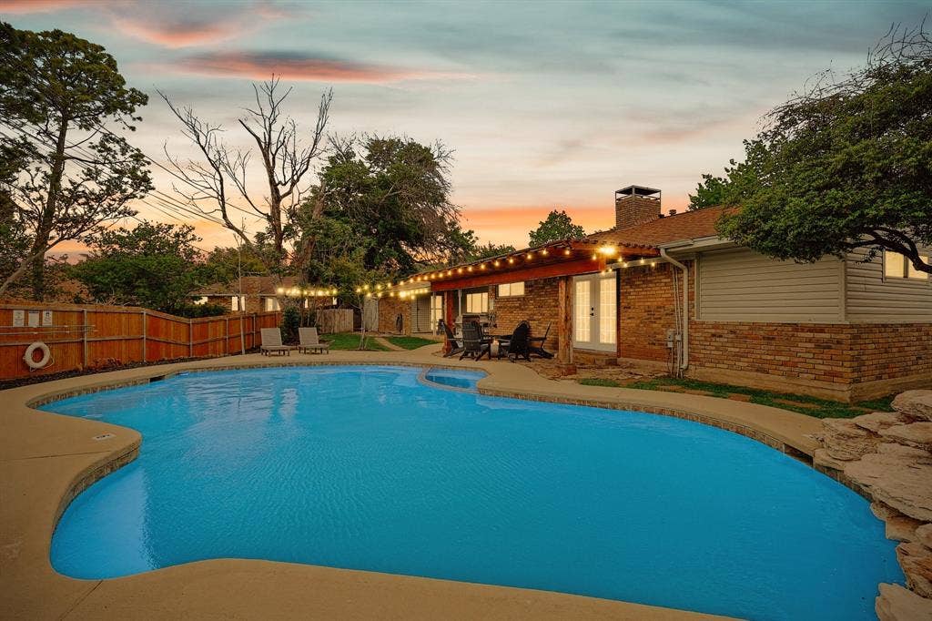 1208 Mayleaf Drive, Irving, TX 75060 Resort-style backyard featuring a freeform swimming pool, concrete patio, and a brick exterior with white French doors