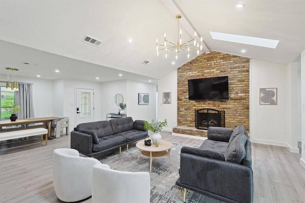 1208 Mayleaf Drive, Irving, TX 75060 Vaulted ceiling living area featuring a brick fireplace surround, wood-finish flooring, recessed lighting, and a skylight