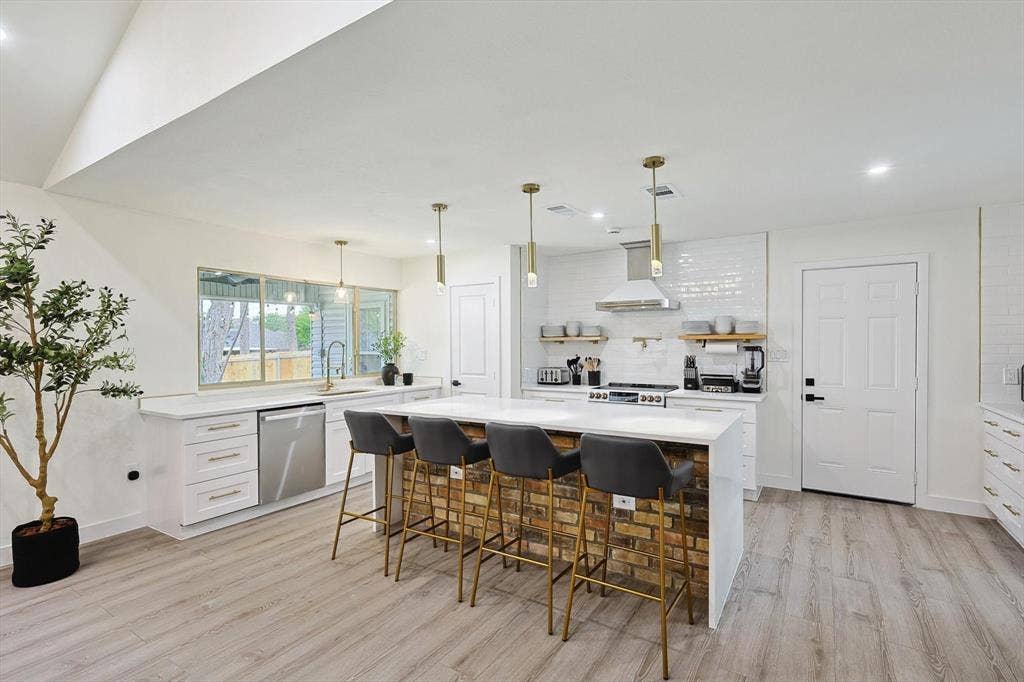 1208 Mayleaf Drive, Irving, TX 75060 Open-concept kitchen featuring an expansive island with a brick-finish base, integrated stainless steel appliances, white subway tile backsplash, and wood-finish flooring