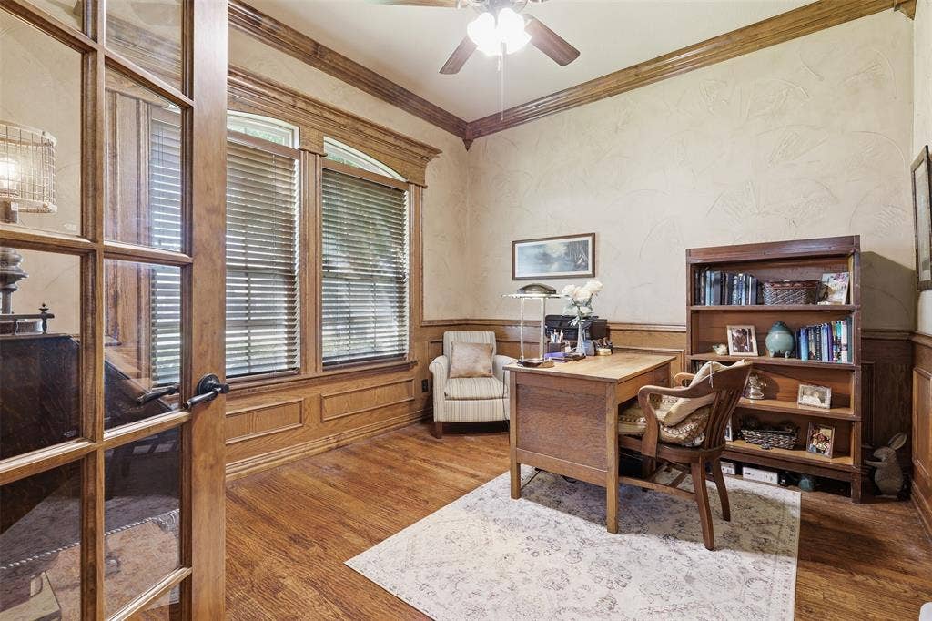 Dedicated room featuring hardwood flooring, extensive wood trim, wainscoting, and a ceiling fan