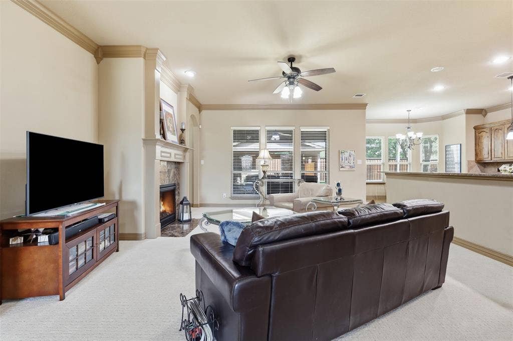 Living area featuring a stone-surround fireplace, crown molding, a ceiling fan, recessed lighting, and multiple windows