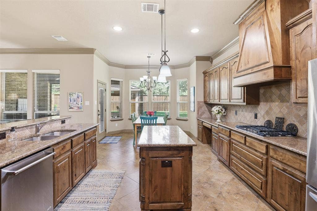 Expansive kitchen featuring wood-finish cabinetry, speckled granite countertops, and a full tile backsplash