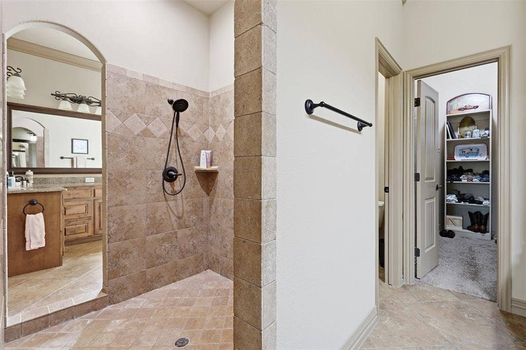 Walk-in shower with tiled walls and flooring, featuring a dark-finish showerhead and built-in shelf