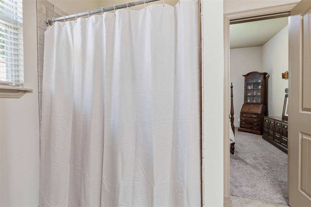 Shower with a tiled surround, a window featuring horizontal blinds, and a neutral color palette