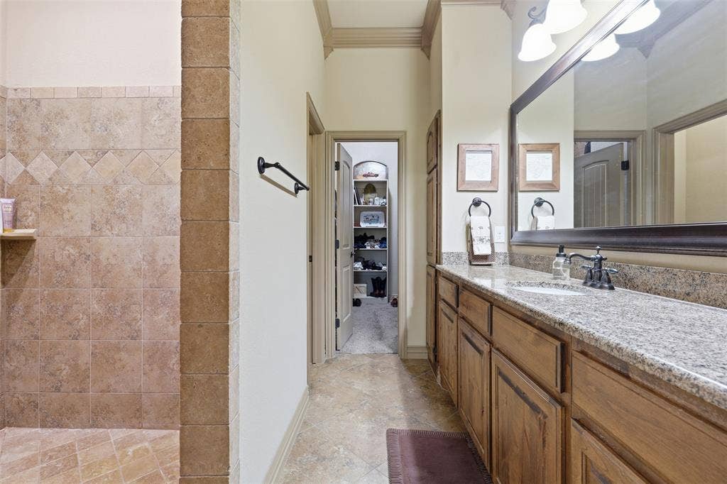 Bathroom with a stone-finish tile shower, extended vanity with granite-finish countertop, dark wood-finish cabinetry, and a large framed mirror