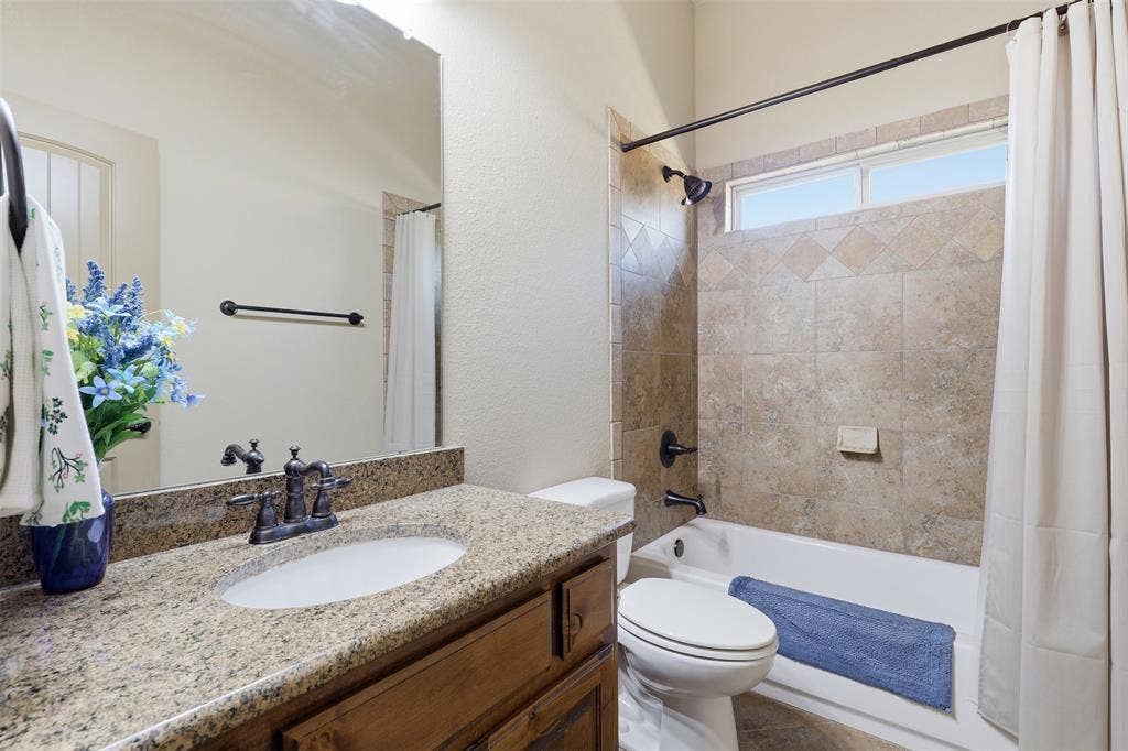 Bathroom featuring a granite-finish countertop with an undermount sink, dark bronze-finish fixtures, a large vanity mirror, a bathtub with a tiled surround, and transom windows above the tub