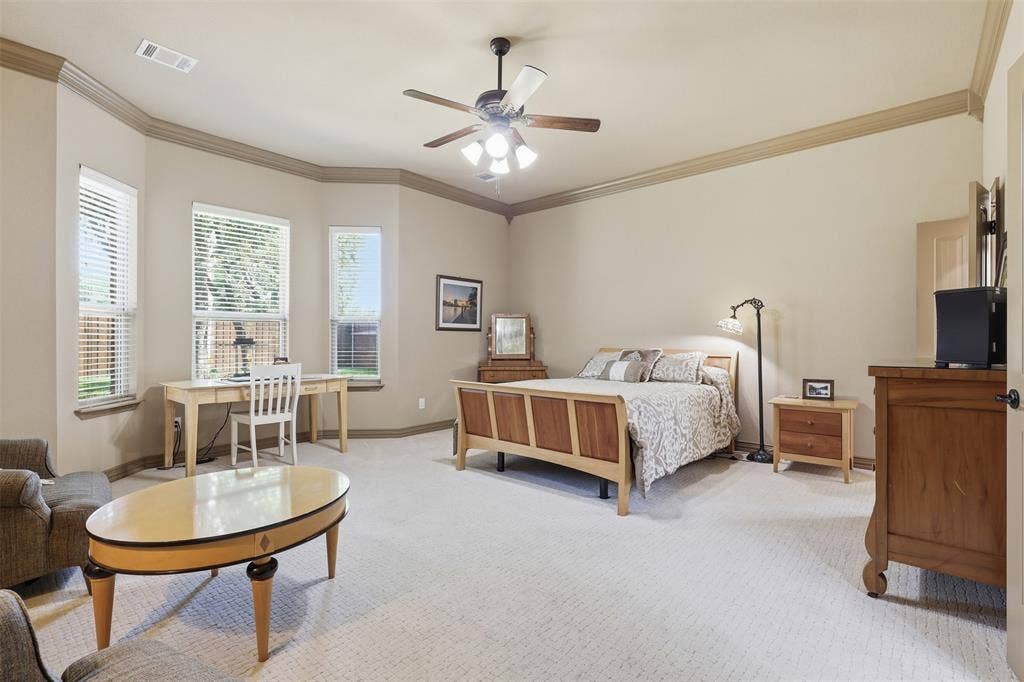 Spacious bedroom featuring light-colored carpet flooring, a ceiling fan with integrated lighting, and multiple windows with horizontal blinds