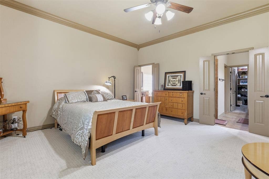 Spacious room featuring light-colored walls with crown molding, soft carpeting, and a ceiling fan with integrated lighting