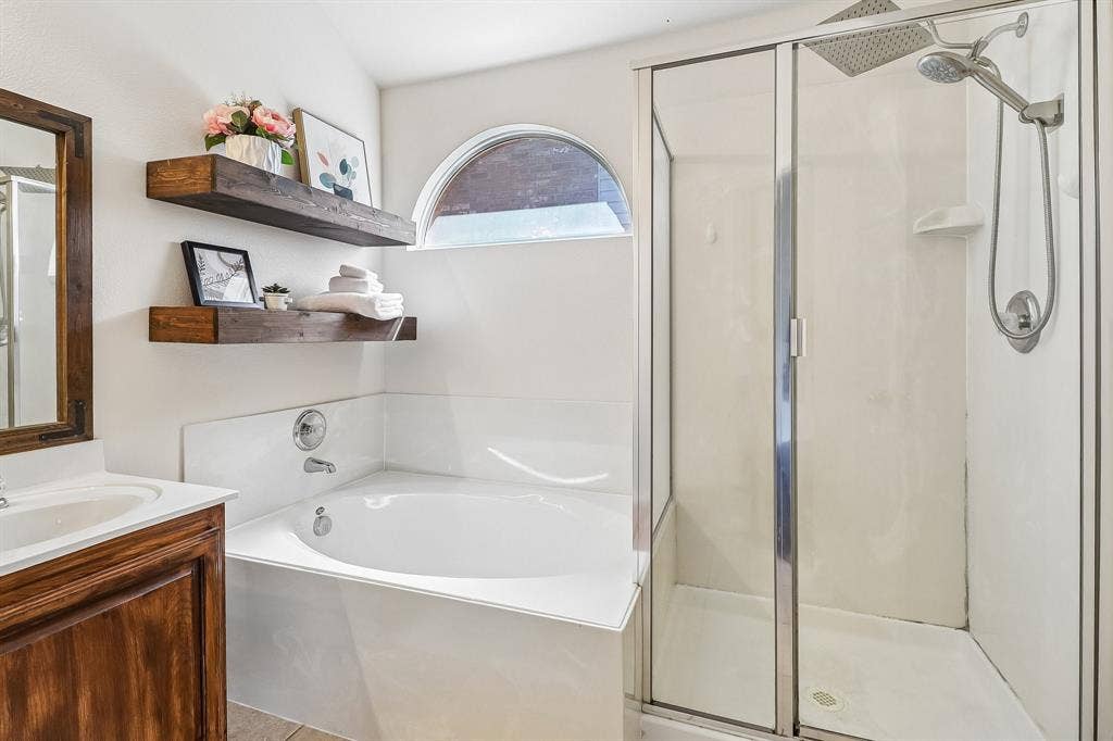 Bathroom featuring a corner soaking tub, a separate glass-enclosed shower with a rain shower head, and an arched window