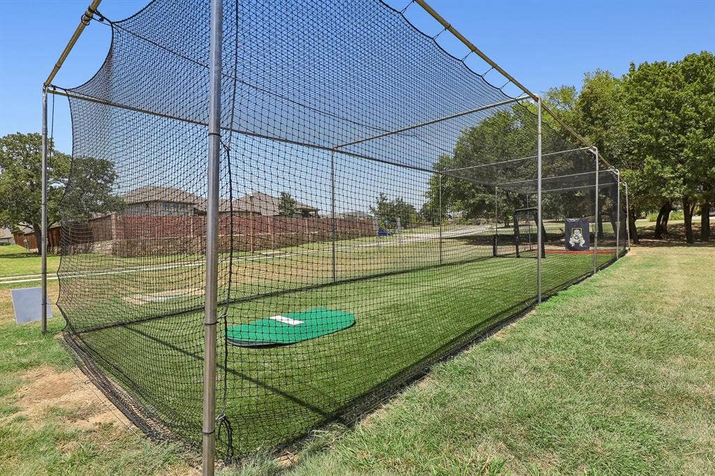 Outdoor batting cage with a full net enclosure, metal frame, artificial turf flooring, and a green home plate mat