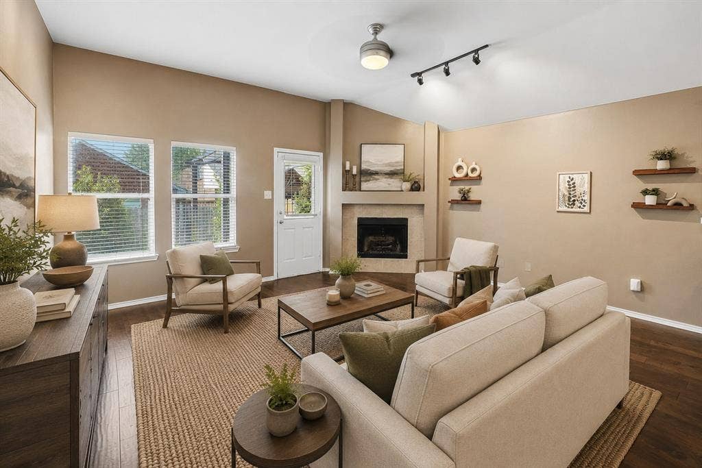 Living area featuring wood-finish flooring, a corner fireplace with a mantel, and multiple windows with blinds.Virtual Staging