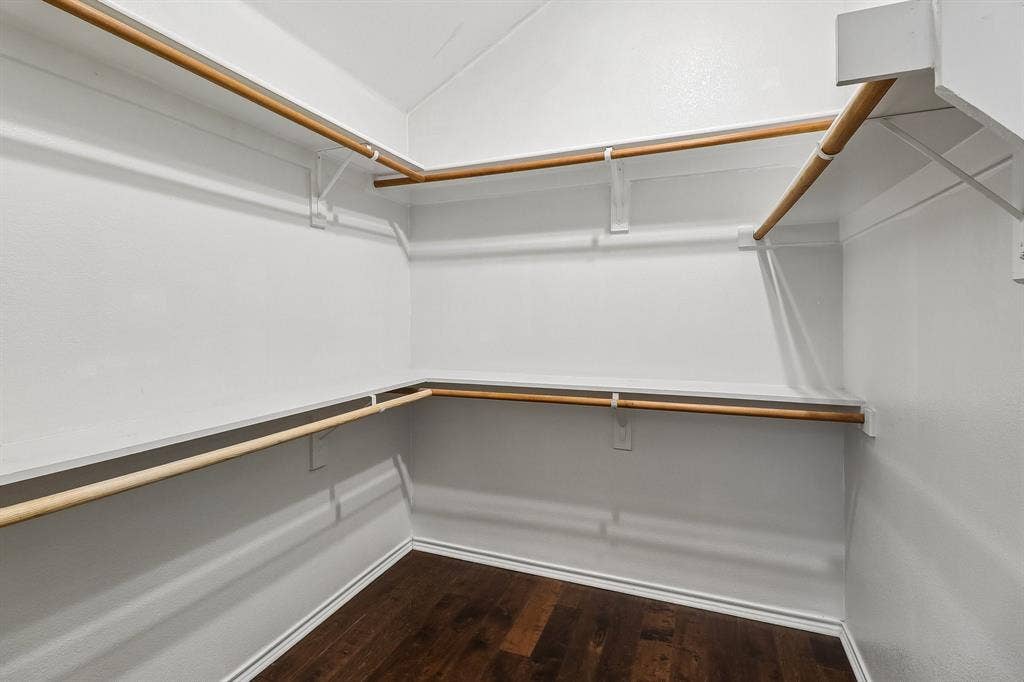 Spacious walk-in closet featuring wood-finish flooring, white walls, multiple shelving units, and ample hanging rods