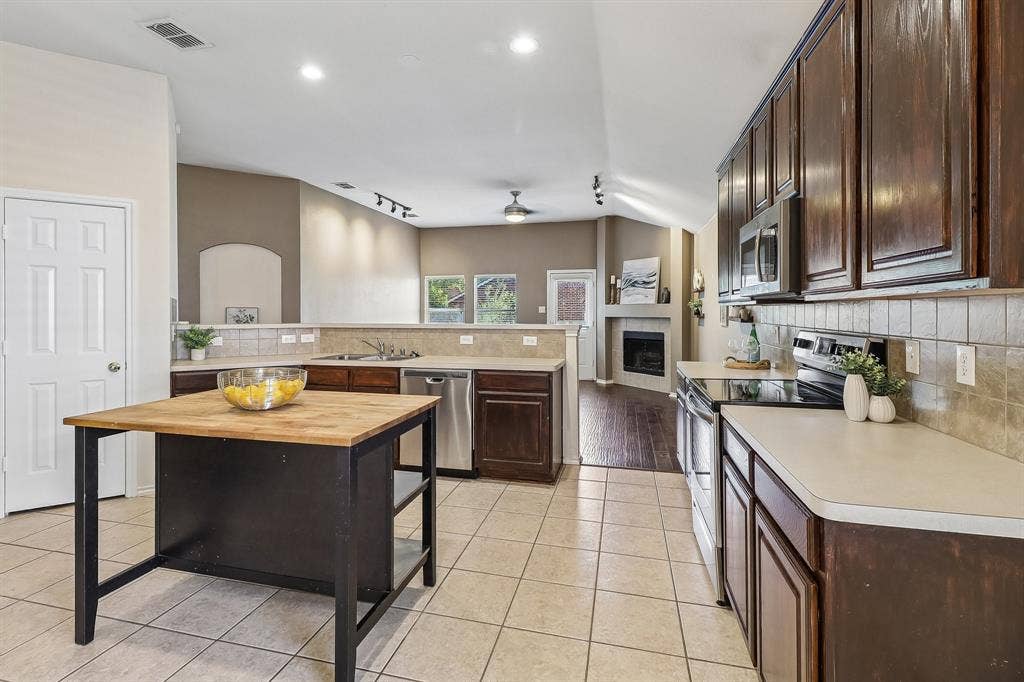 Spacious kitchen featuring dark wood cabinetry, stainless steel appliances, tile flooring, and a central island with a wood-finish countertop